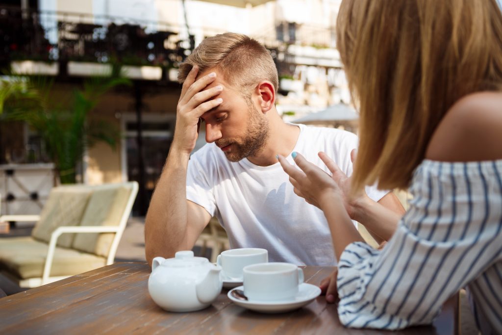Young beautiful couple drinking tea, speaking, quarreling, sitting in cafe