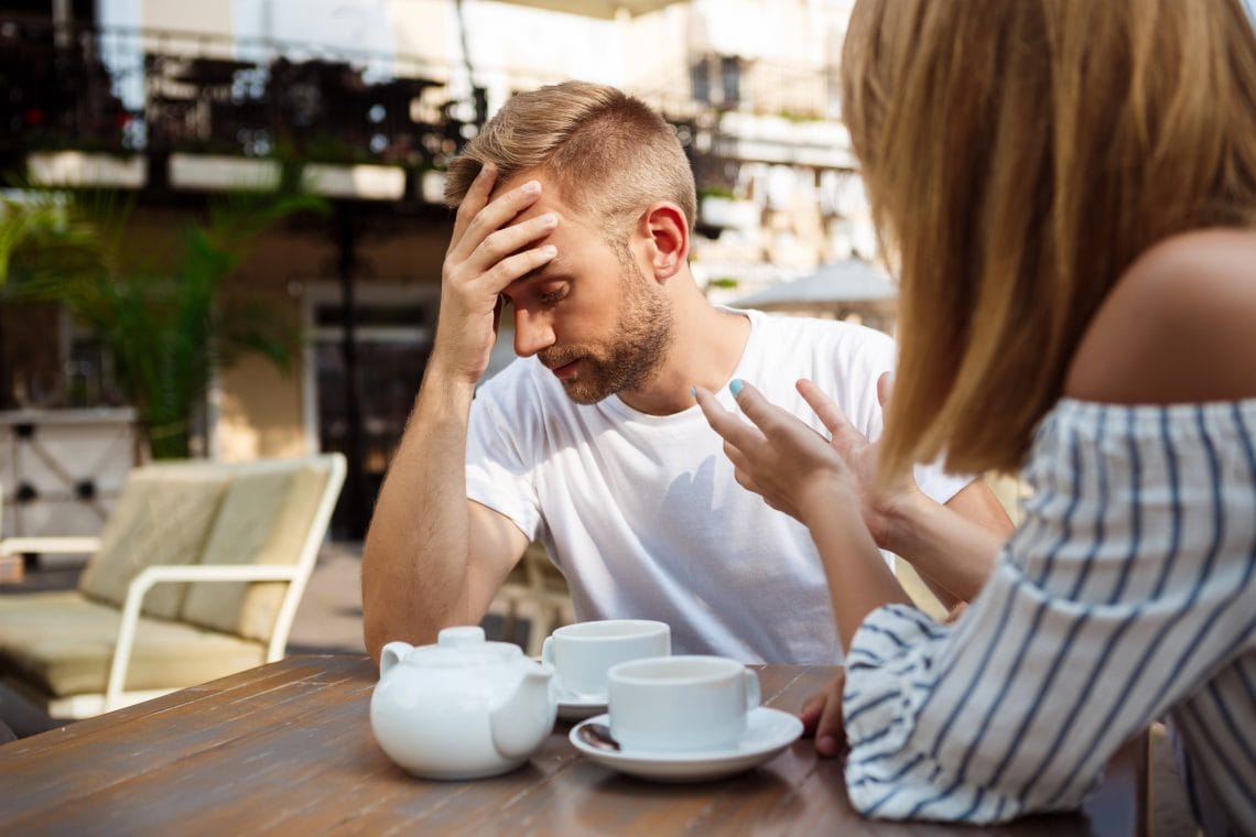 Young beautiful couple drinking tea, speaking, quarreling, sitting in cafe