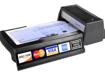 Máquina decalcadora de cartão de crédito manual, conhecida como "knuckle-buster", sobre um fundo branco. O aparelho é preto e mostra os logotipos da Discover, MasterCard, Visa e American Express.