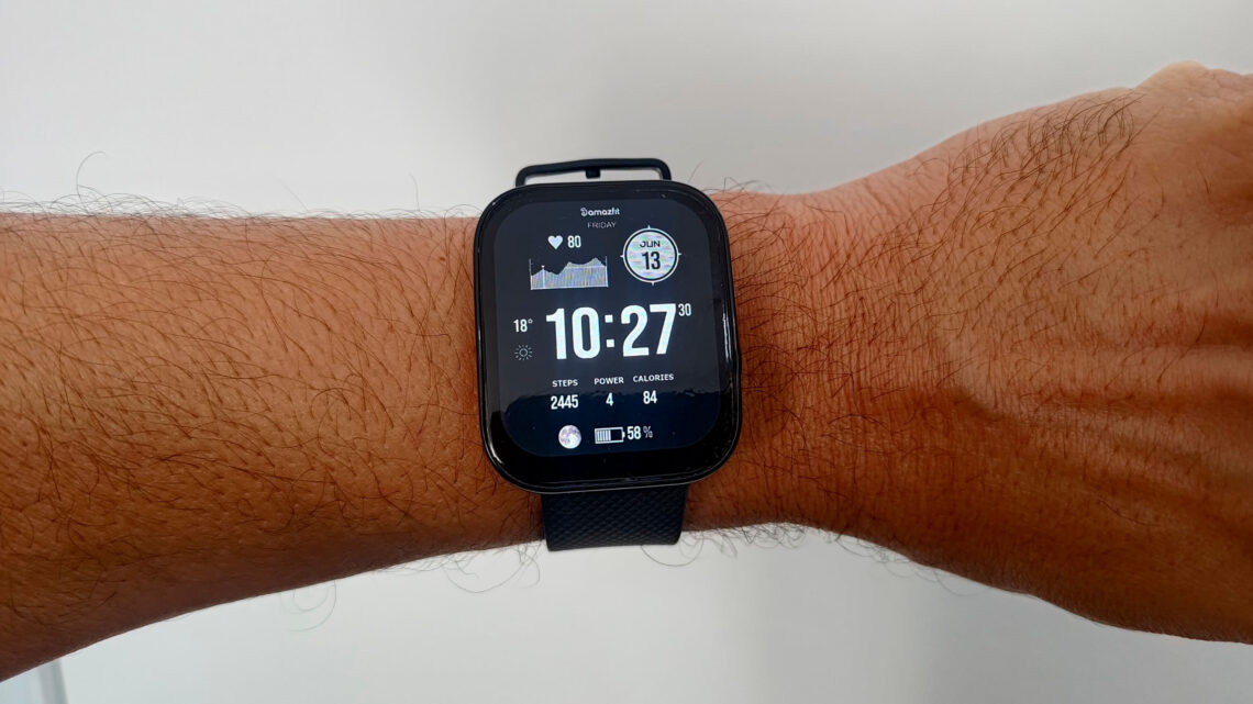 O smartwatch Amazfit Bip 5 Pro visto de perto no pulso, destacando seu design quadrado e a tela LCD exibindo o mostrador principal com horas e dados de atividade física.