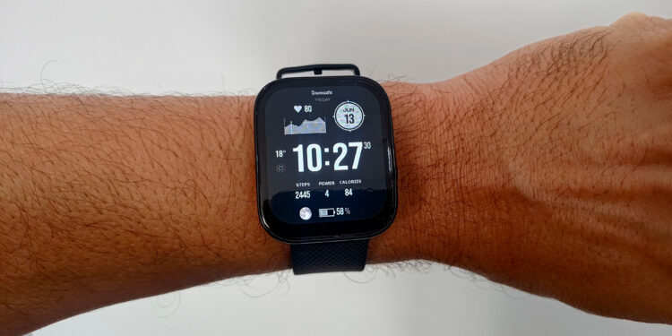 O smartwatch Amazfit Bip 5 Pro visto de perto no pulso, destacando seu design quadrado e a tela LCD exibindo o mostrador principal com horas e dados de atividade física.