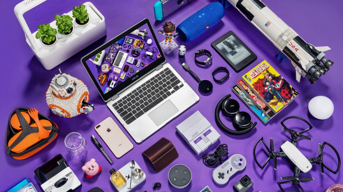 Uma coleção de gadgets e itens de cultura pop arranjados sobre uma superfície roxa, incluindo um laptop, smartphone, drone e console de videogame, ilustrando o tema da dependência tecnológica.