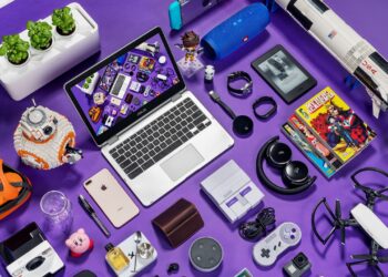 Uma coleção de gadgets e itens de cultura pop arranjados sobre uma superfície roxa, incluindo um laptop, smartphone, drone e console de videogame, ilustrando o tema da dependência tecnológica.