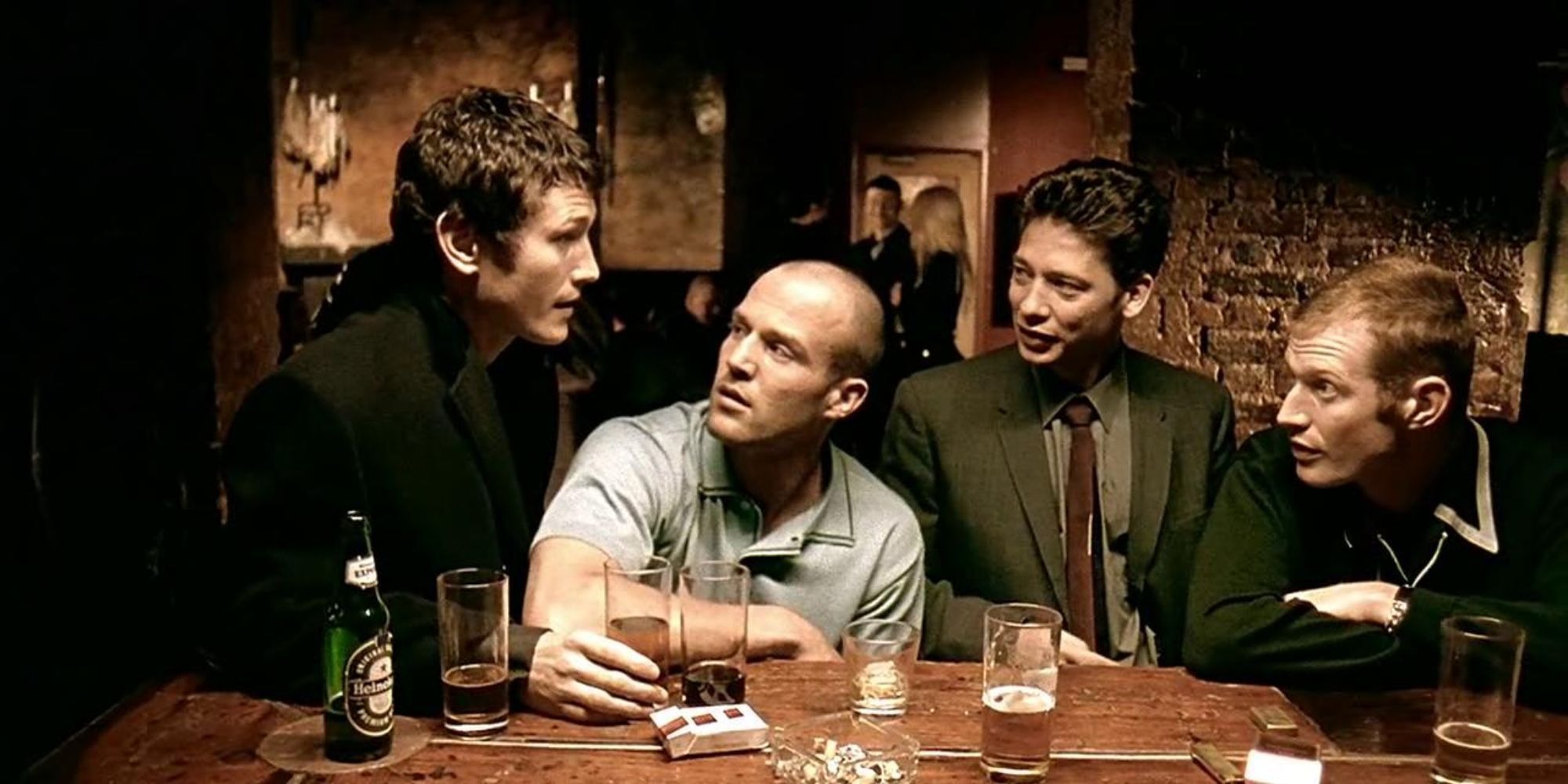 Os quatro protagonistas do filme Jogos, Trapaças e Dois Canos Fumegantes sentados em um bar, em uma cena do filme de Guy Ritchie.