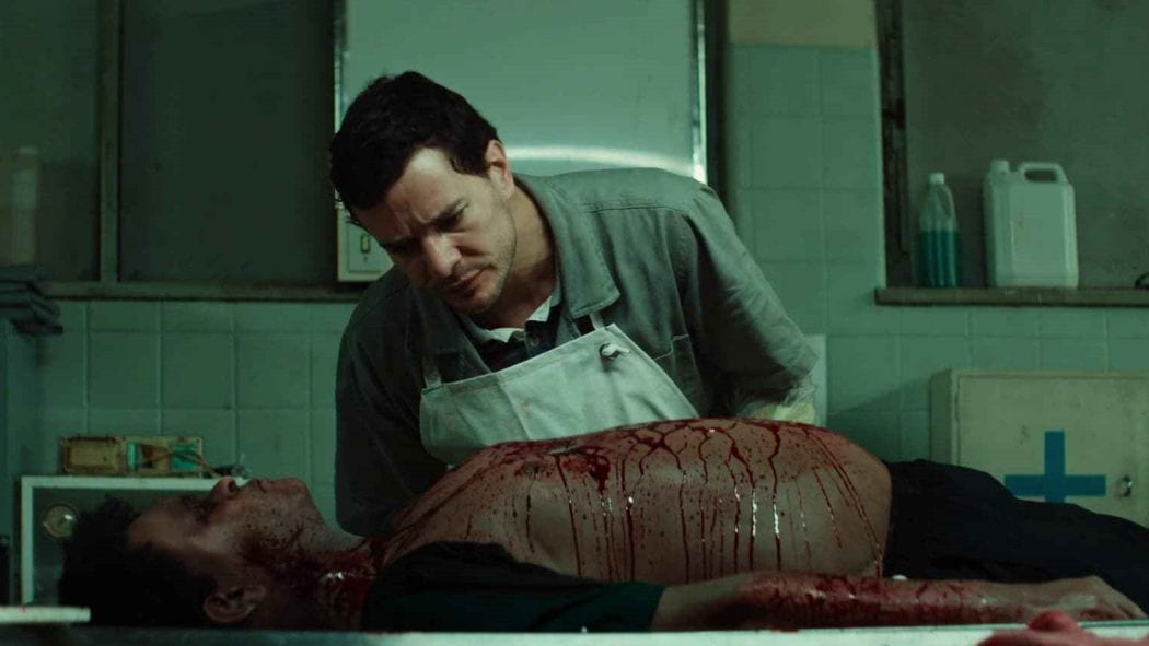 Cena do filme de terror brasileiro Morto Não Fala, com o personagem Stênio (Daniel de Oliveira) se comunicando com um cadáver em um necrotério.