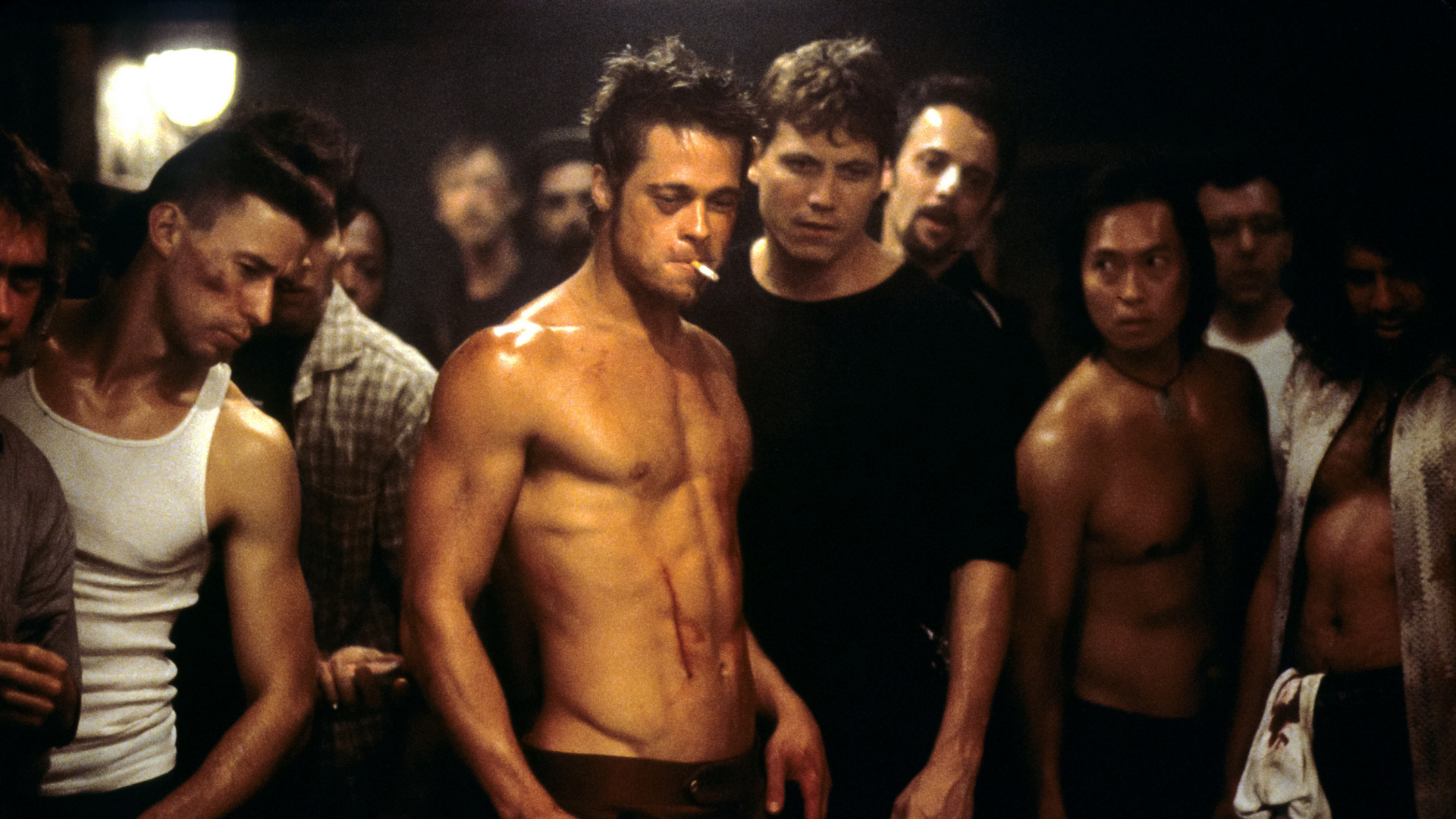 Cena do filme Clube da Luta mostrando Tyler Durden, interpretado por Brad Pitt, sem camisa e com um cigarro na boca, ao lado do Narrador, vivido por Edward Norton, em uma das reuniões do clube.