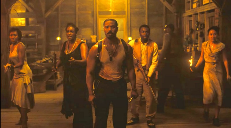 Michael B. Jordan como protagonista do filme Pecadores, em uma cena de alta tensão, liderando um grupo de pessoas em um local escuro iluminado por tochas.