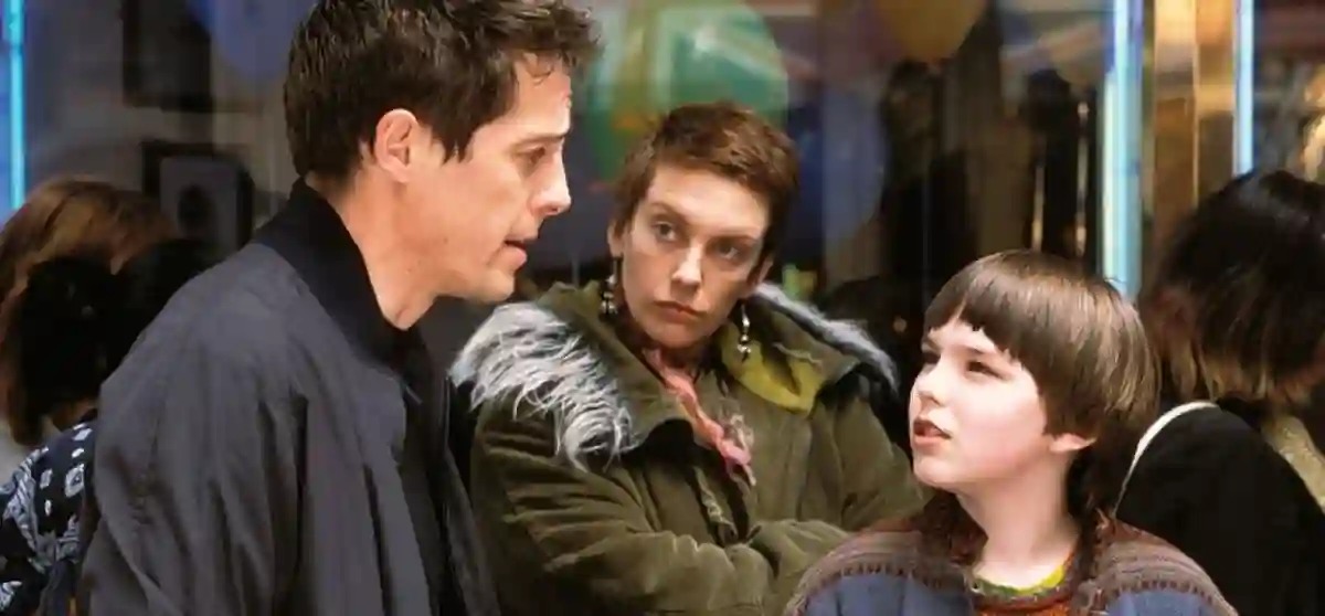Cena do filme Um Grande Garoto, com os personagens Will (Hugh Grant), Fiona (Toni Collette) e Marcus (Nicholas Hoult) conversando em uma loja.