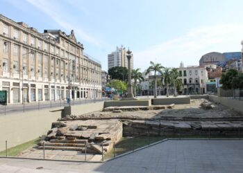 Vista do sítio arqueológico do Cais do Valongo, no Rio de Janeiro, com as ruínas de pedra em primeiro plano e os prédios da Zona Portuária ao fundo.