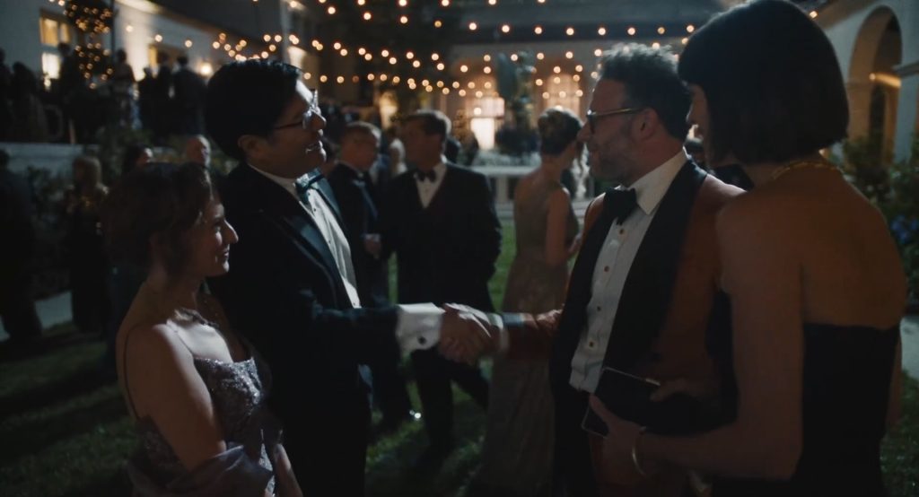 Cena da série O Estúdio: Matt Remick (Seth Rogen), vestindo um terno marrom, cumprimenta um homem de smoking em uma festa de gala.