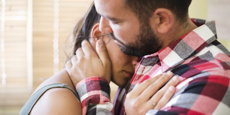 Um homem abraça uma mulher, confortando-a. Ele segura seu rosto com as mãos, demonstrando apoio e carinho em um momento de tristeza ou dificuldade.