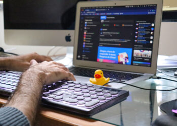 Homem digitando em um teclado com um pato de borracha amarelo em cima de um notebook, fazendo alusão ao aplicativo Kwack que emite sons de pato.