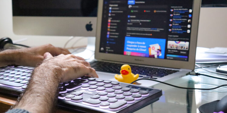 Homem digitando em um teclado com um pato de borracha amarelo em cima de um notebook, fazendo alusão ao aplicativo Kwack que emite sons de pato.