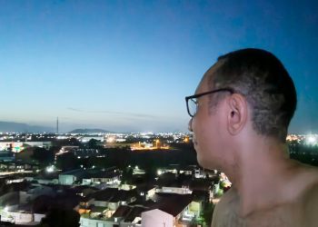 Homem de óculos, em perfil, olhando para o horizonte de uma cidade ao anoitecer, em um momento de reflexão sobre a jornada de autoconhecimento.