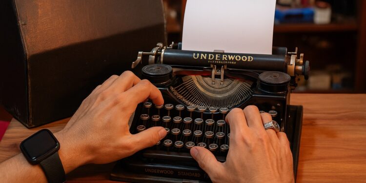 Close-up das mãos de um homem digitando em uma máquina de escrever Underwood preta e antiga sobre uma mesa de madeira.