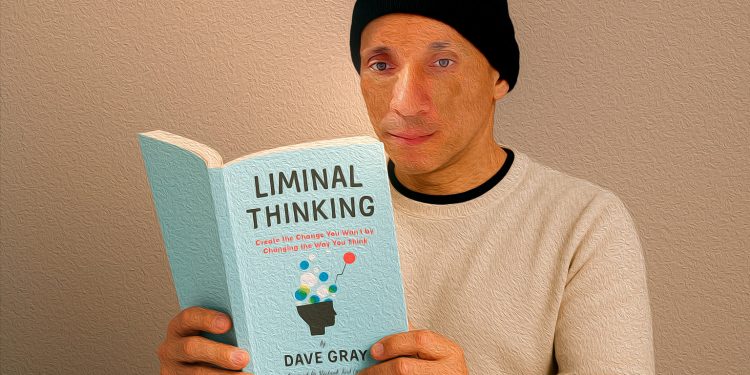 Homem de touca preta e blusa clara lê atentamente o livro 'Liminal Thinking' de Dave Gray, segurando-o com as duas mãos em frente a um fundo neutro.