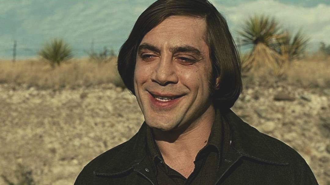 Javier Bardem como o psicopata Anton Chigurh no filme 'Onde os Fracos Não Têm Vez', sorrindo de forma sinistra no deserto.