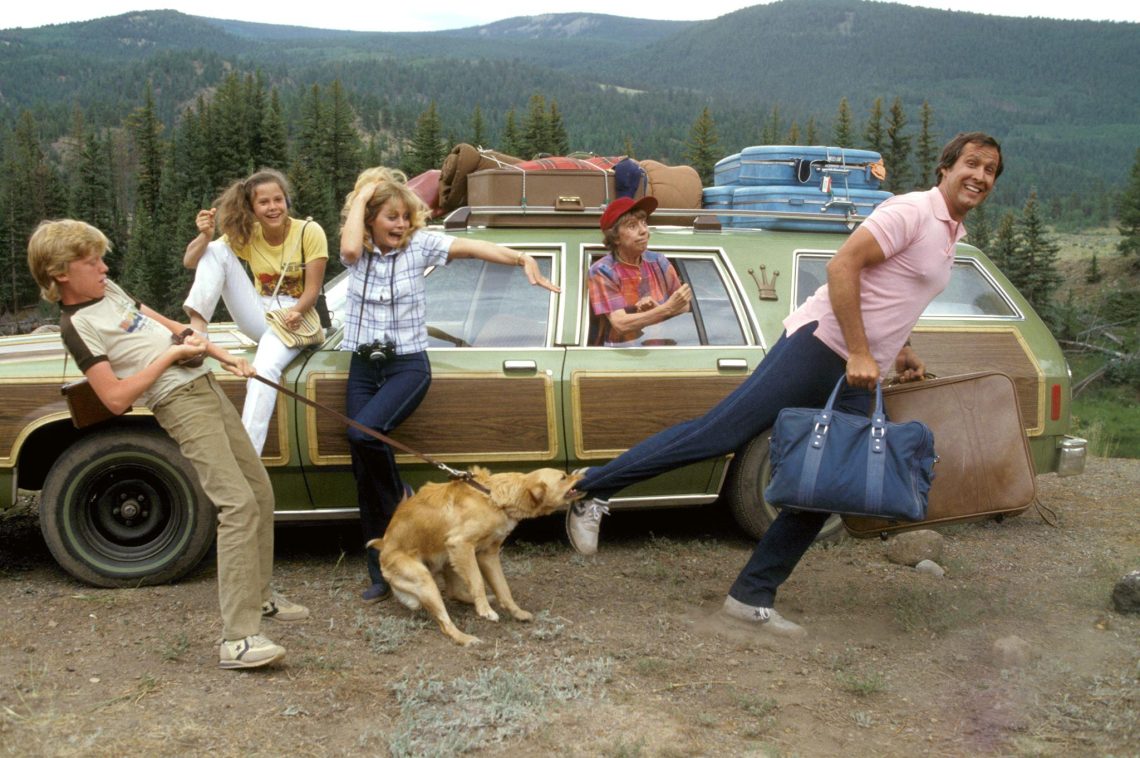 A família Griswold do filme Férias Frustradas em uma cena caótica ao lado do seu carro verde, ilustrando o estresse que pode ser o início de uma viagem de férias.