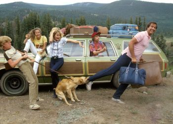 A família Griswold do filme Férias Frustradas em uma cena caótica ao lado do seu carro verde, ilustrando o estresse que pode ser o início de uma viagem de férias.