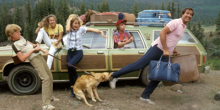 A família Griswold do filme Férias Frustradas em uma cena caótica ao lado do seu carro verde, ilustrando o estresse que pode ser o início de uma viagem de férias.