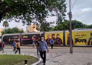 VLT no Rio de Janeiro com anúncio da série The Boys, enquanto pessoas caminham pela calçada em um fim de tarde, representando o palco de histórias do cotidiano.