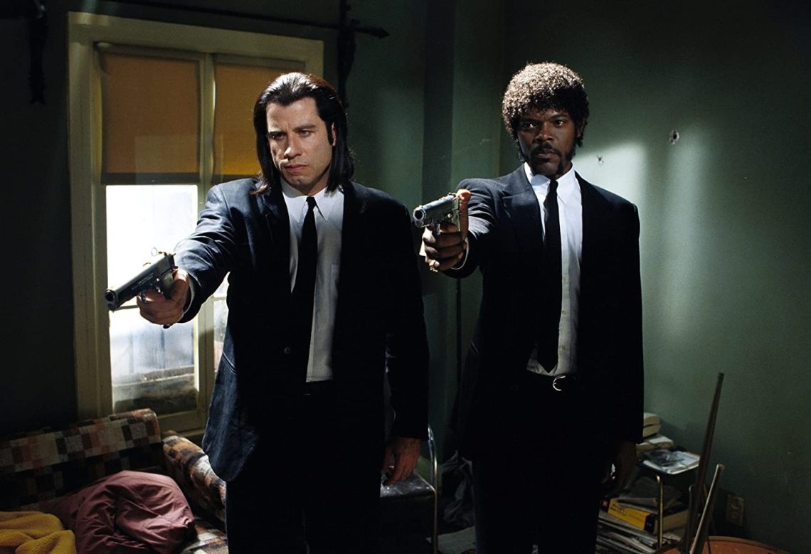 Jules Winnfield e Vincent Vega, personagens de Pulp Fiction, vestidos com ternos pretos, apontando suas pistolas para a frente em uma cena icônica do filme.