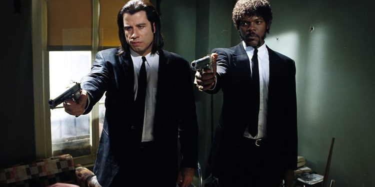 Jules Winnfield e Vincent Vega, personagens de Pulp Fiction, vestidos com ternos pretos, apontando suas pistolas para a frente em uma cena icônica do filme.