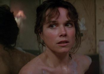 A atriz Barbara Hershey como Carla Moran no filme 'O Enigma do Mal', olhando assustada para algo fora de quadro dentro de um banheiro.