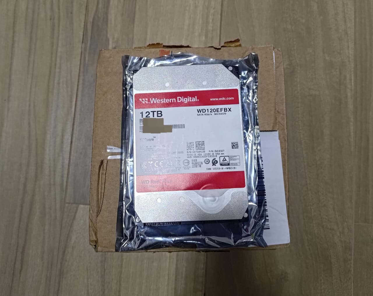 HD de 12TB da marca Western Digital em sua embalagem plástica antiestática, sobre uma caixa de papelão.