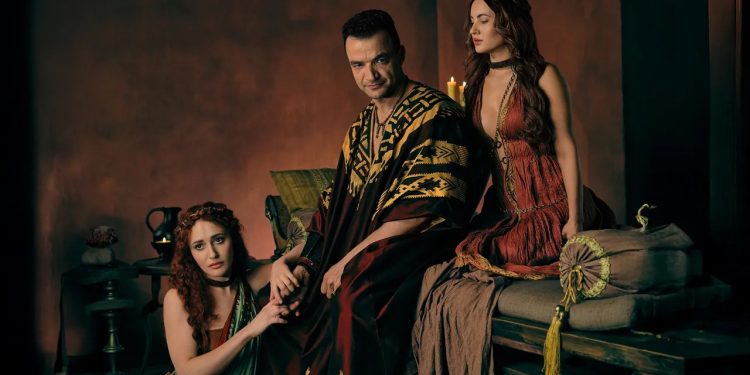 Nick E. Tarabay como Ashur sentado em um trono, ladeado por duas mulheres com vestes romanas, em uma cena promocional da série Spartacus: House of Ashur.