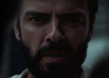 Close-up do rosto de Gleb (Anton Lapenko) no filme Um Homem de Sucesso, com expressão intensa de medo e tensão em ambiente escuro.