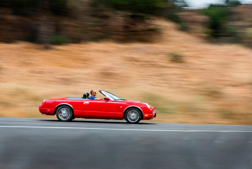 Robert dirigindo um carro conversível vermelho em alta velocidade, ilustrando a metáfora de assumir o controle das metas e da produtividade.