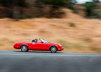 Robert dirigindo um carro conversível vermelho em alta velocidade, ilustrando a metáfora de assumir o controle das metas e da produtividade.