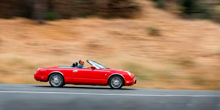 Robert dirigindo um carro conversível vermelho em alta velocidade, ilustrando a metáfora de assumir o controle das metas e da produtividade.