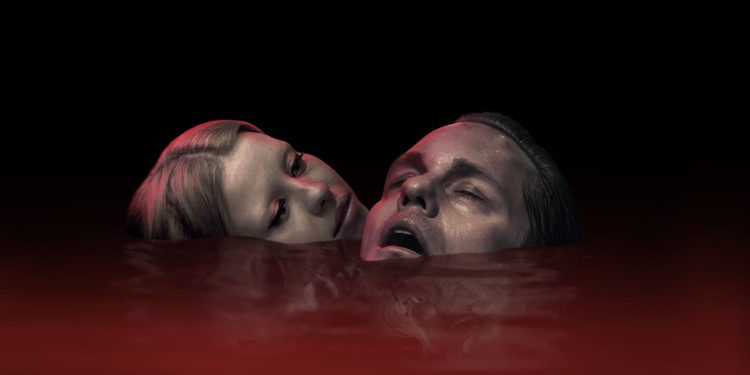 Close-up dos atores Mia Goth e Alexander Skarsgård com os rostos emergindo de um líquido vermelho escuro, em uma cena do filme Piscina Infinita. Título da Imagem: Mia Goth e Alexander Skarsgård - Piscina Infinita