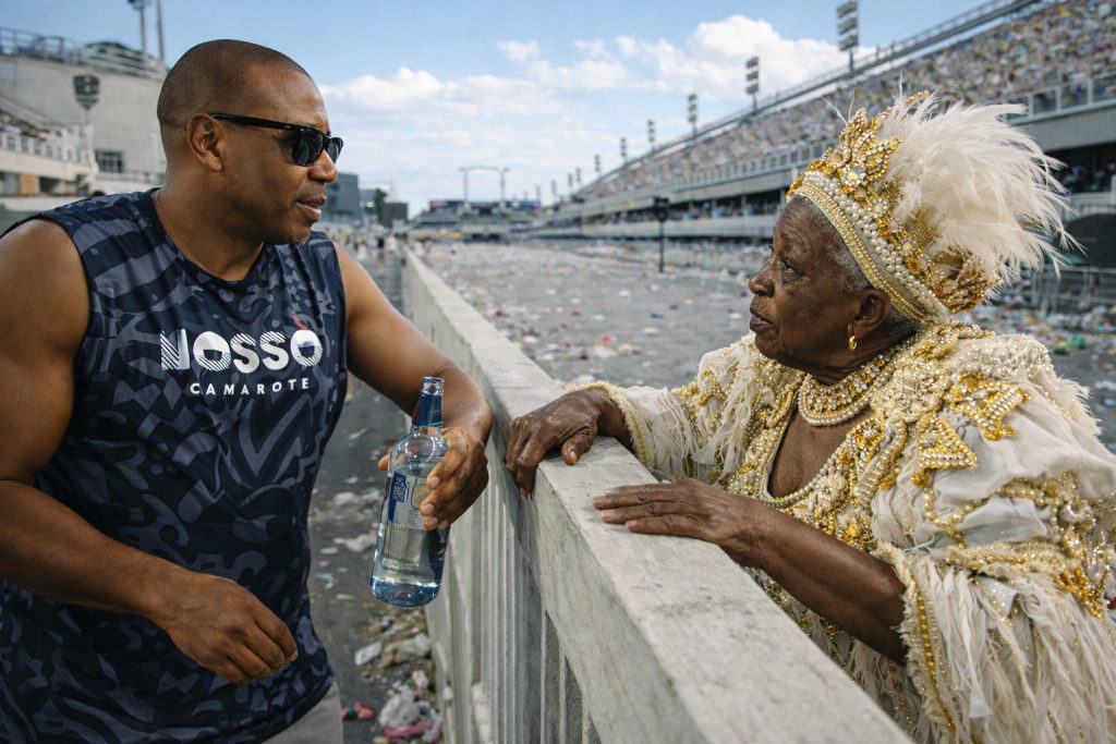 Robert, vestindo o abadá do "Nosso Camarote", conversa com uma senhora da Velha Guarda na beira da pista da Sapucaí.