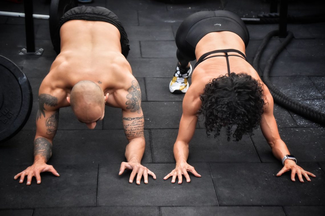 Homem e mulher em posição de prancha no treino de crossfit mostrando a força e a funcionalidade do corpo humano.