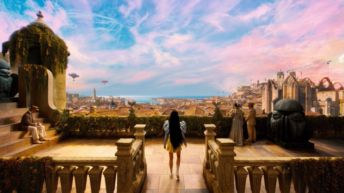 Personagem Bella Baxter de costas, observando uma paisagem surreal e colorida de uma cidade com balões no céu, em uma cena do filme Pobres Criaturas, representando a descoberta e a experimentação do mundo.